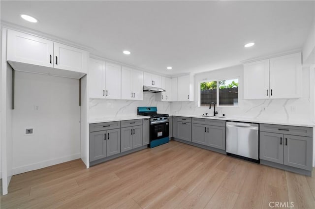 kitchen featuring appliances with stainless steel finishes, a sink, light wood-style flooring, under cabinet range hood, and gray cabinetry