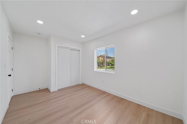 unfurnished bedroom with baseboards, a closet, recessed lighting, and light wood-style flooring