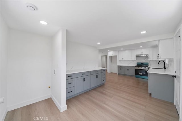 kitchen with recessed lighting, gray cabinets, under cabinet range hood, stainless steel range with gas stovetop, and a sink