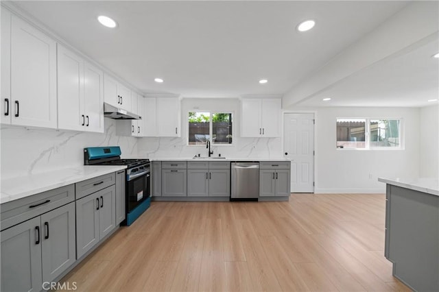 kitchen with gray cabinets, under cabinet range hood, a sink, light wood finished floors, and appliances with stainless steel finishes