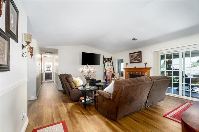 living area with lofted ceiling, light wood finished floors, a fireplace, and baseboards