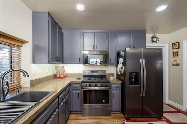 kitchen featuring stainless steel appliances, a sink, recessed lighting, gray cabinets, and light wood-style flooring
