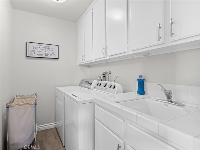 laundry room featuring wood finished floors, baseboards, separate washer and dryer, a sink, and cabinet space