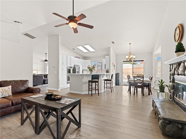 living area with high vaulted ceiling, ceiling fan with notable chandelier, light wood-type flooring, and visible vents