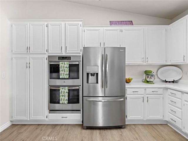 kitchen featuring stainless steel appliances, vaulted ceiling, white cabinetry, and light wood-type flooring
