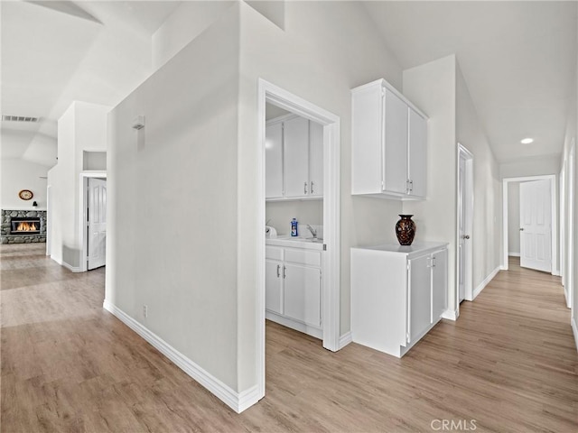 corridor featuring baseboards, visible vents, a sink, and light wood finished floors
