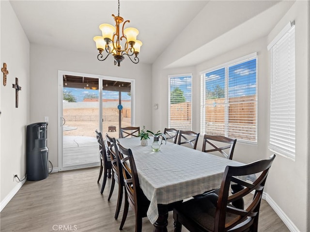 dining space featuring baseboards, lofted ceiling, a chandelier, and light wood-type flooring
