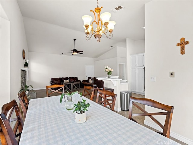 dining area with visible vents, ceiling fan with notable chandelier, baseboards, wood finished floors, and vaulted ceiling