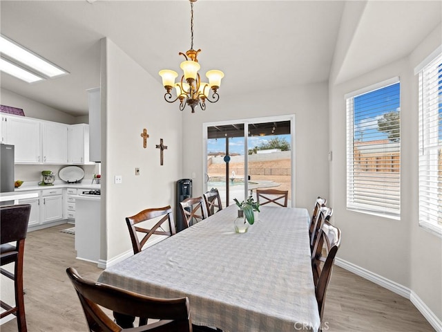 dining room with baseboards, a notable chandelier, light wood-style flooring, and lofted ceiling