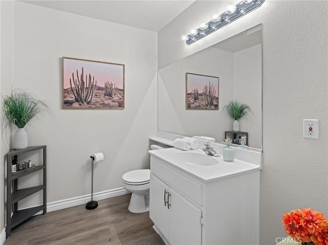 half bathroom featuring vanity, baseboards, toilet, and wood finished floors