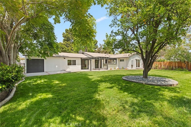 rear view of house featuring a lawn, fence, and a garage