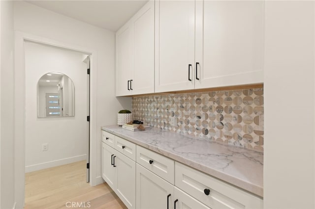 kitchen with decorative backsplash, light wood-style flooring, white cabinetry, and light stone countertops