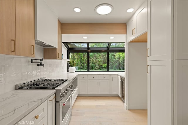 kitchen with decorative backsplash, light stone countertops, white cabinetry, stainless steel range, and light wood-style flooring