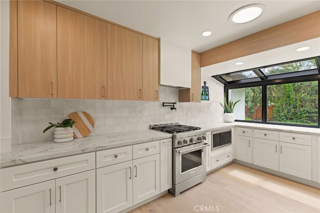 kitchen with light stone countertops, appliances with stainless steel finishes, light wood-style floors, white cabinetry, and decorative backsplash