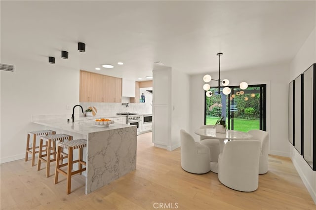 kitchen with a peninsula, a breakfast bar, light wood-type flooring, and tasteful backsplash