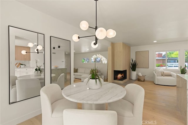 dining area with baseboards, an inviting chandelier, light wood finished floors, and a fireplace