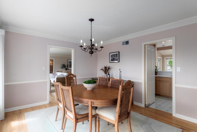 dining area with visible vents, baseboards, light wood finished floors, an inviting chandelier, and ornamental molding