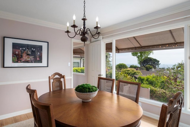 dining space featuring light wood-style floors, baseboards, crown molding, and a notable chandelier
