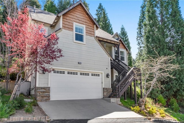view of front of house featuring roof with shingles, stairs, an attached garage, stone siding, and driveway