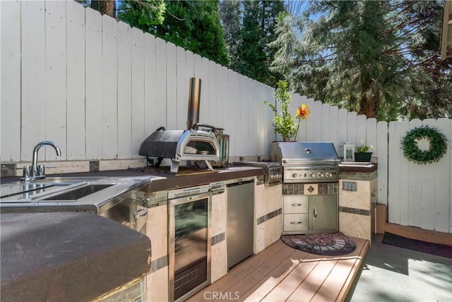 view of patio / terrace featuring fence, a sink, beverage cooler, area for grilling, and an outdoor kitchen