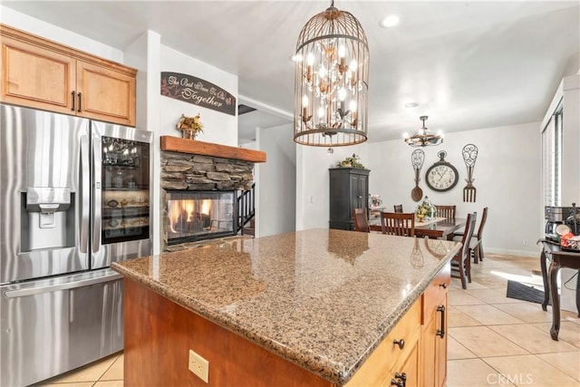 kitchen featuring stainless steel fridge, a center island, light stone counters, light tile patterned floors, and a notable chandelier