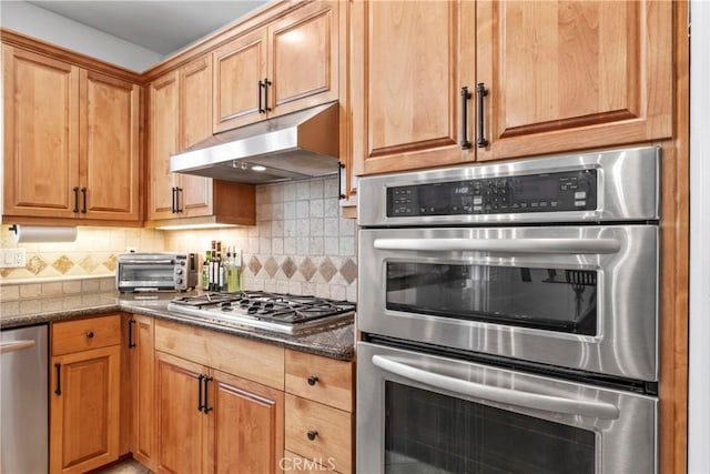kitchen featuring appliances with stainless steel finishes, dark stone counters, decorative backsplash, a toaster, and under cabinet range hood