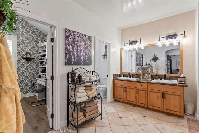 bathroom with double vanity, toilet, wallpapered walls, and a sink