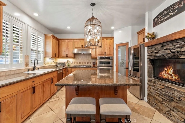 kitchen with a kitchen island, appliances with stainless steel finishes, a sink, light tile patterned floors, and under cabinet range hood