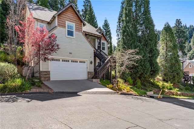 view of home's exterior with stairs, a shingled roof, stone siding, a garage, and driveway