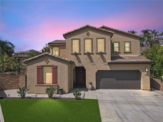 mediterranean / spanish-style home with a garage, driveway, a tiled roof, stucco siding, and a front lawn