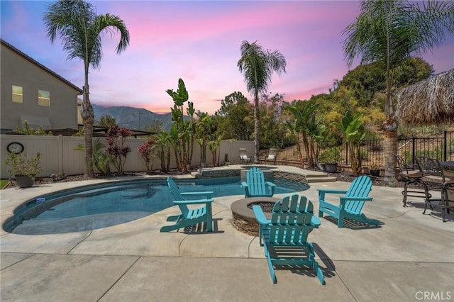 pool at dusk with a fenced backyard, a patio area, and a mountain view