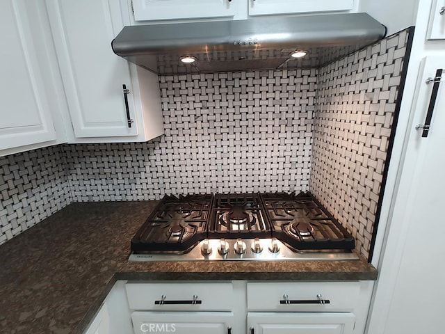 interior details with backsplash, dark countertops, white cabinets, stainless steel gas stovetop, and under cabinet range hood