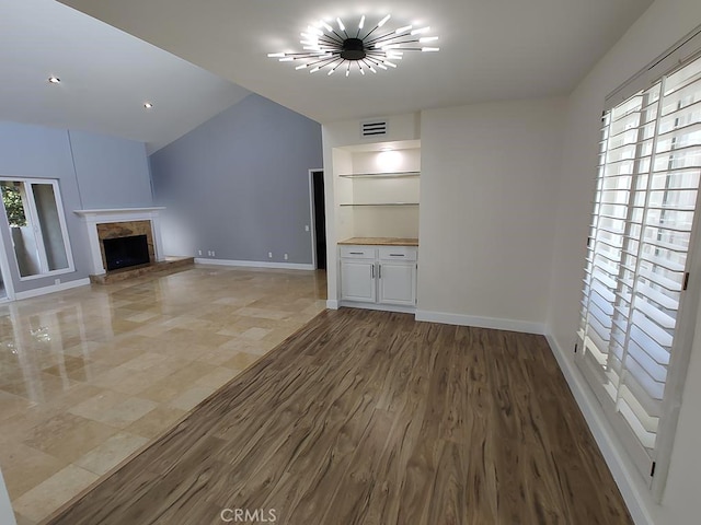 unfurnished living room with visible vents, vaulted ceiling, light wood-type flooring, baseboards, and a fireplace with raised hearth