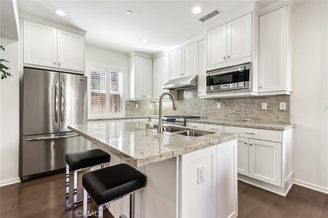 kitchen featuring appliances with stainless steel finishes, under cabinet range hood, decorative backsplash, dark wood-style flooring, and white cabinetry