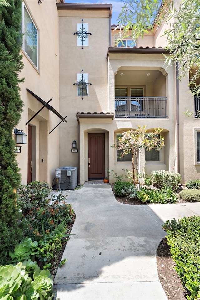 property entrance with central AC unit, a balcony, and stucco siding