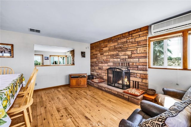 living area featuring a wall mounted air conditioner, a stone fireplace, hardwood / wood-style floors, baseboards, and visible vents