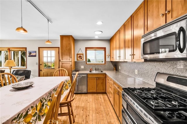 kitchen with brown cabinetry, a sink, appliances with stainless steel finishes, backsplash, and decorative light fixtures