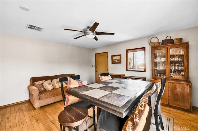 dining area featuring visible vents, light wood-style floors, ceiling fan, and baseboards