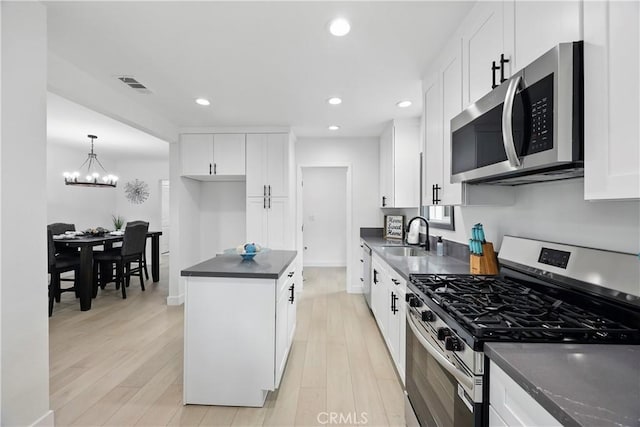 kitchen with an inviting chandelier, dark countertops, a sink, light wood-style flooring, and stainless steel appliances