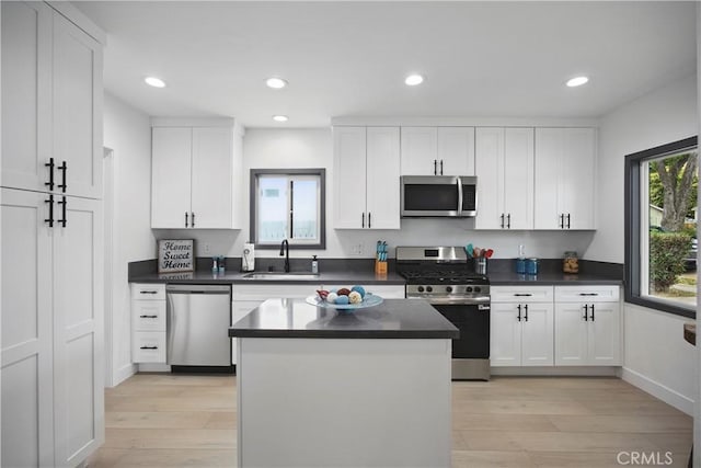 kitchen featuring white cabinets, dark countertops, a sink, light wood finished floors, and stainless steel appliances
