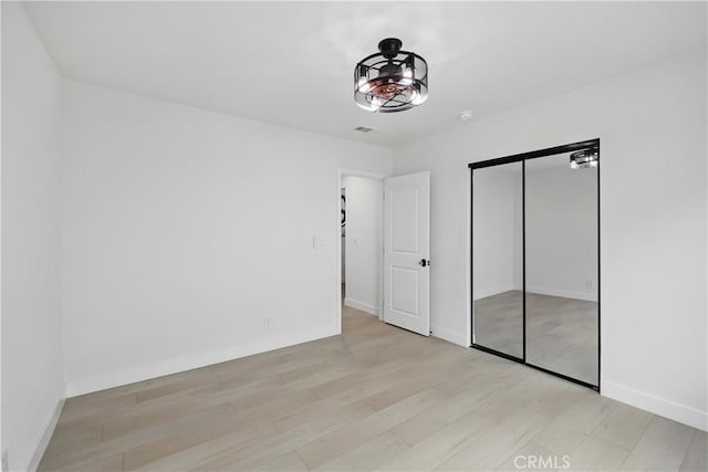 unfurnished bedroom featuring light wood-style floors, baseboards, a closet, and visible vents