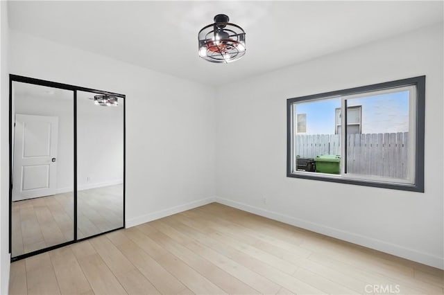 unfurnished bedroom with baseboards, light wood-style flooring, and a closet