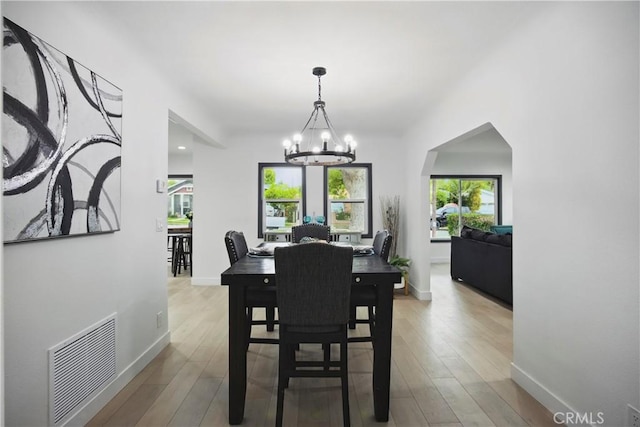 dining space featuring an inviting chandelier, baseboards, wood finished floors, and visible vents