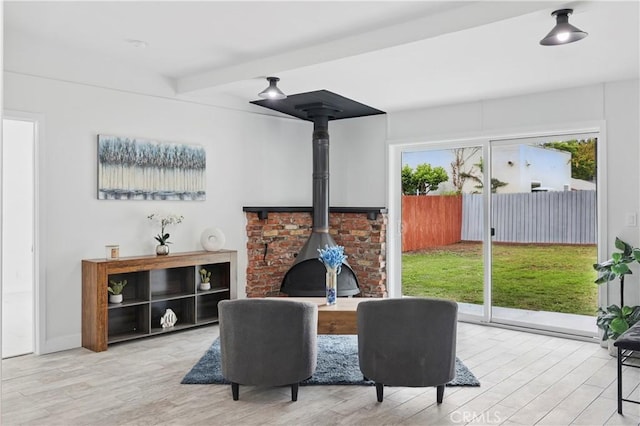 living area featuring beam ceiling, a wood stove, and wood finished floors