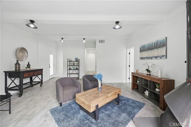 living room featuring visible vents, light wood-style flooring, and beamed ceiling