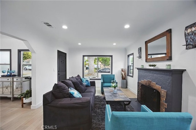 living area with a fireplace, light wood-style floors, arched walkways, recessed lighting, and visible vents
