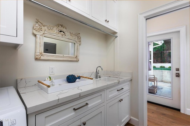 kitchen with washer / clothes dryer, light stone countertops, wood finished floors, a sink, and white cabinets