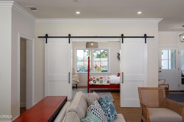 interior space featuring wood finished floors, ornamental molding, a barn door, and visible vents
