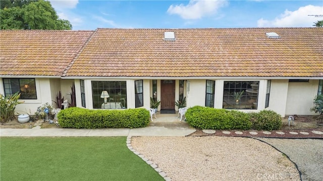 view of front of house featuring a tiled roof, stucco siding, and a front yard