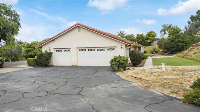 view of front of property featuring stucco siding, an attached garage, a tiled roof, and aphalt driveway